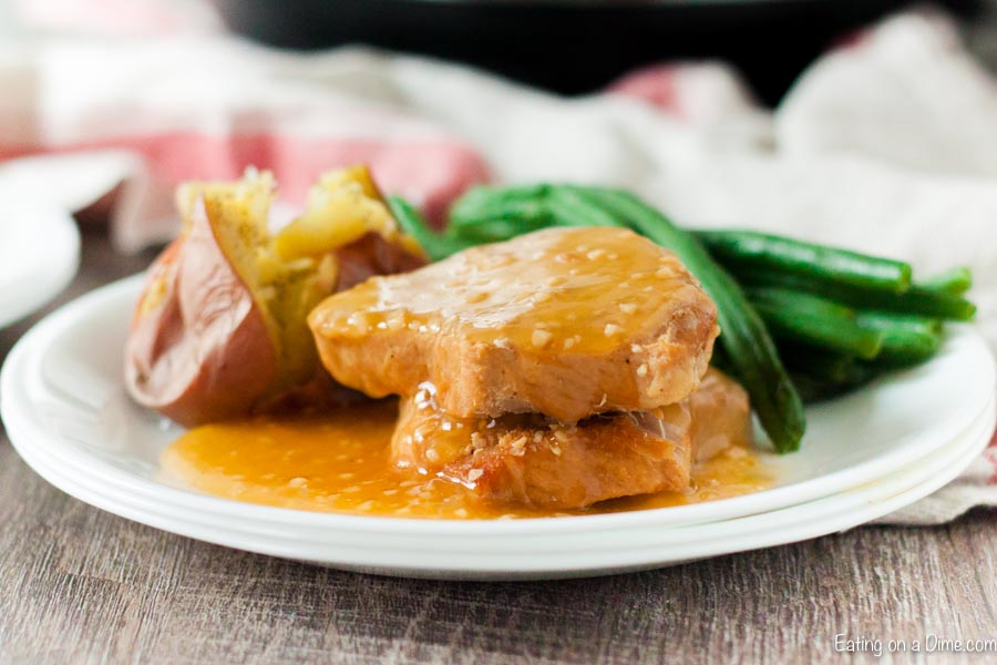 Close up image of honey garlic pork chops on a plate with a bake potato and a side of green beans. 