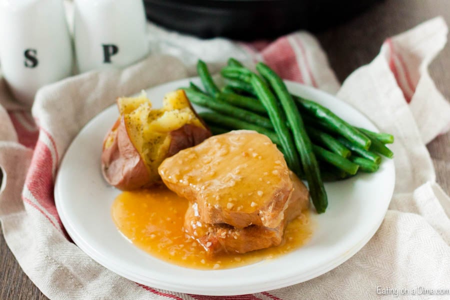 Close up image of honey garlic pork chops on a plate with a bake potato and a side of green beans. 