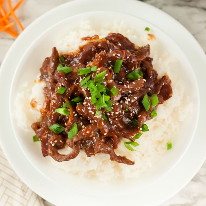 Beef Mongolian on a plate with rice topped with diced green onions