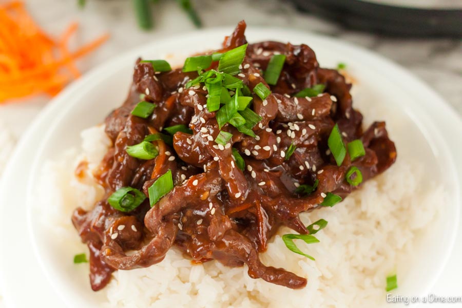 Beef Mongolian on a plate with rice topped with diced green onions. 