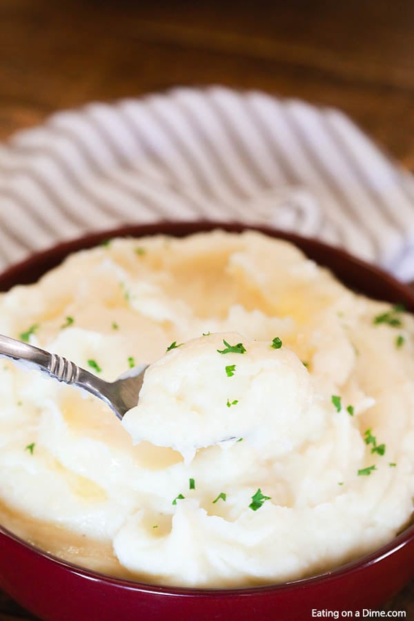 Close up image of mashed potatoes in a red bow with a serving on a spoon. 