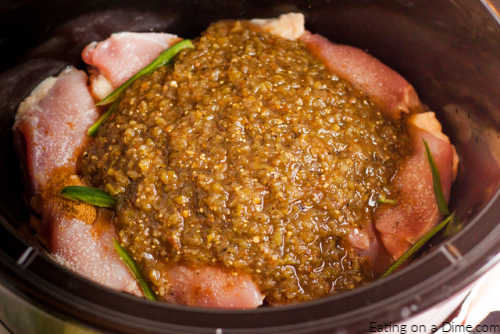 close up image of uncooked chicken in the crock pot topped with salsa verde and sliced jalapenos. 