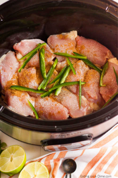 Close up image of uncooked chicken in the crock pot topped with slice jalapenos. 