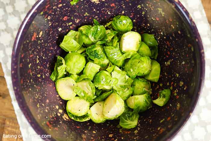 Brussel Sprouts cut in half in a large mixing bowl covered in olive oil and seasoning with salt and pepper 
