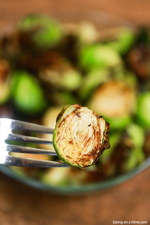 An Air Fryer Roasted Brussel Spout on a fork being served out of a glass bowl 