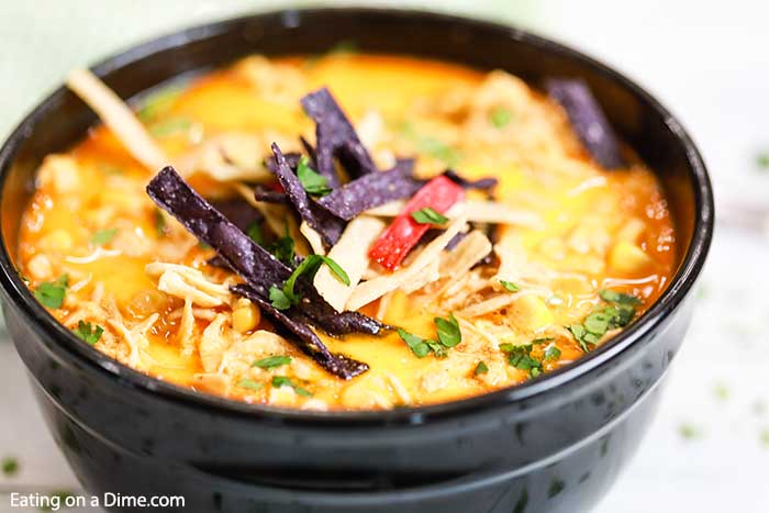 Close up of a bowl of creamy chicken tortilla soup topped with tortilla strips and cilantro with a spoon in it. 