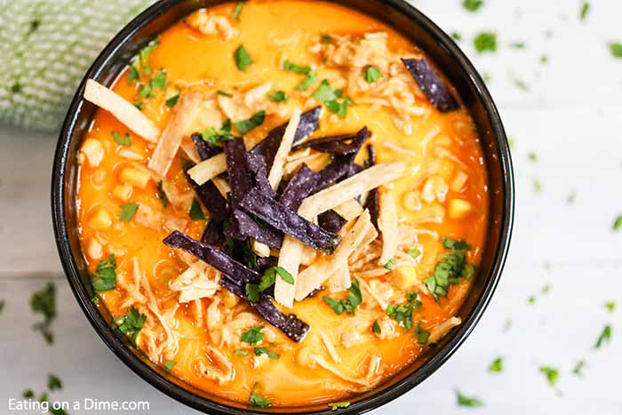 Close up of Bowl of creamy chicken tortilla soup topped with white and purple tortilla strips and cilantro. 