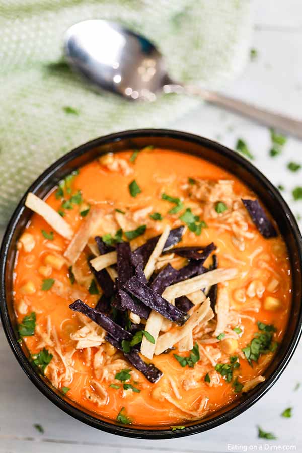 A black Bowl of slow cooker creamy chicken tortilla soup topped with tortilla strips and cilantro. 