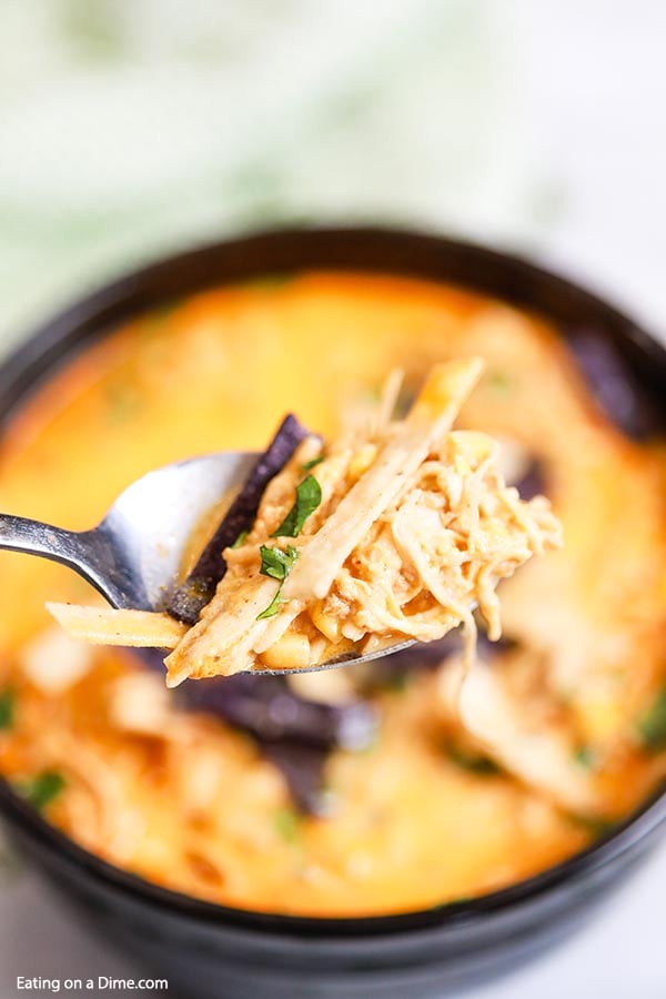 Bowl of creamy chicken tortilla soup topped with tortilla strips and cilantro with a spoon scooping a bite out of the soup. 