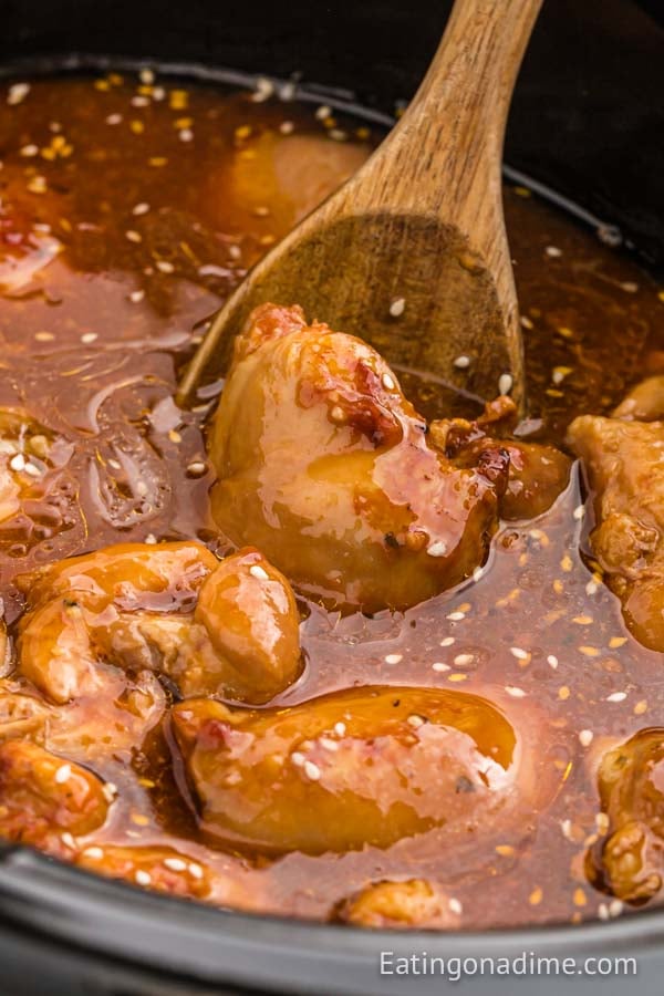 Honey garlic chicken thighs in a crock pot with a wooden spoon