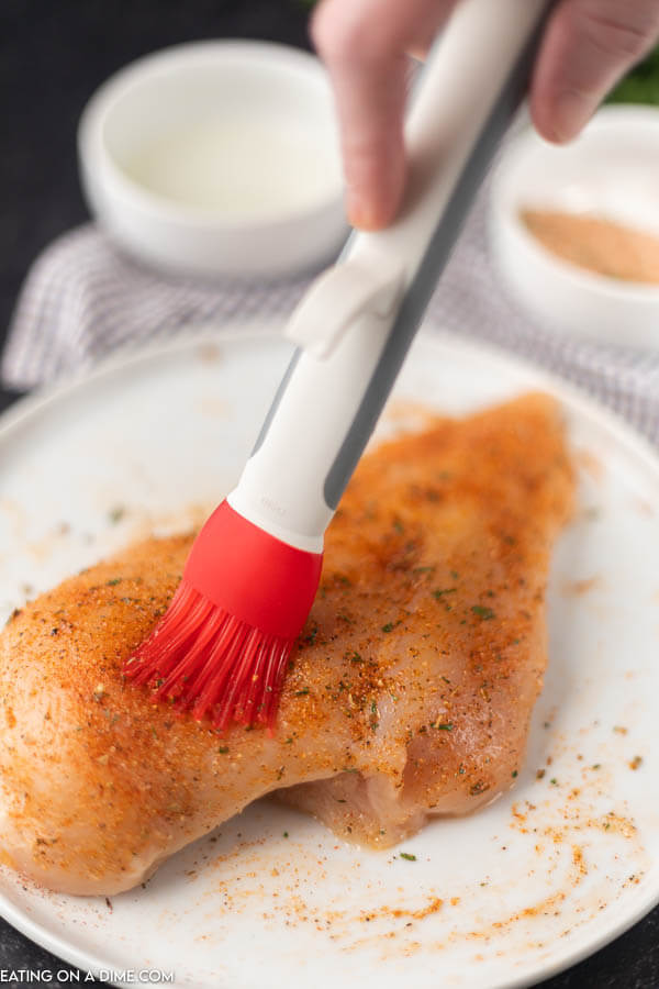 A photo showing the basting brush brushing the seasoning on a chicken breast on a white plate 