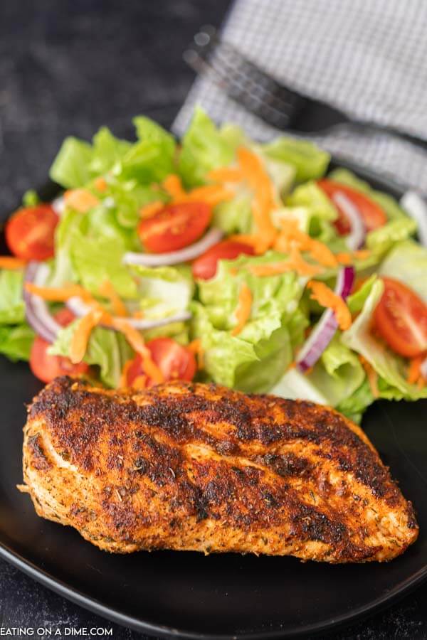 1 blackened chicken breast on a black plate next to a side salad. 