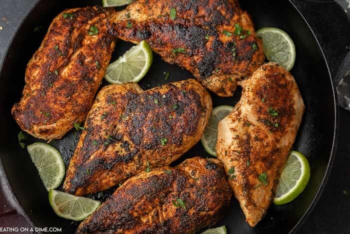 5 pieces of blackened chicken breasts in a cast iron skillet with sliced limes in the pan. 