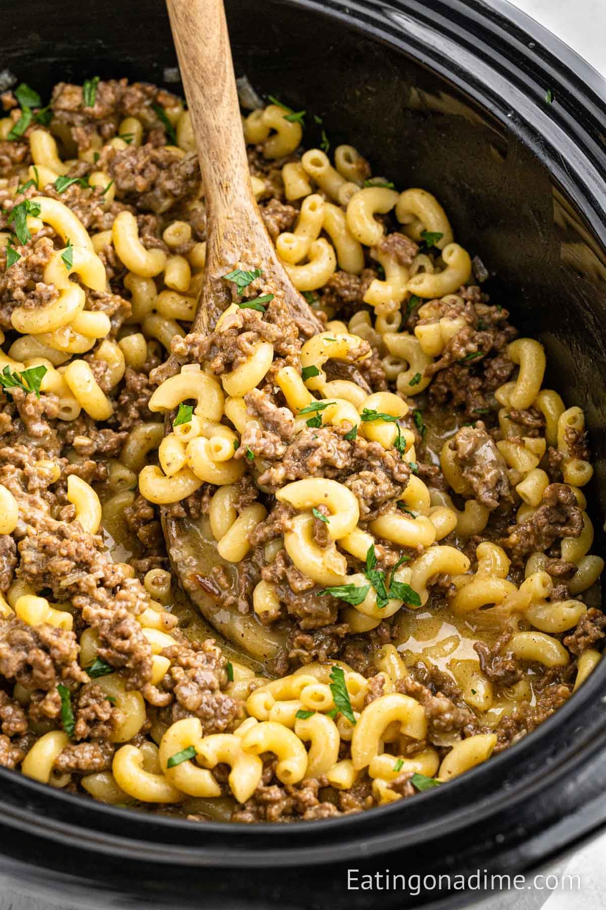 Cheeseburger Macaroni in the slow cooker with a serving on a wooden spoon