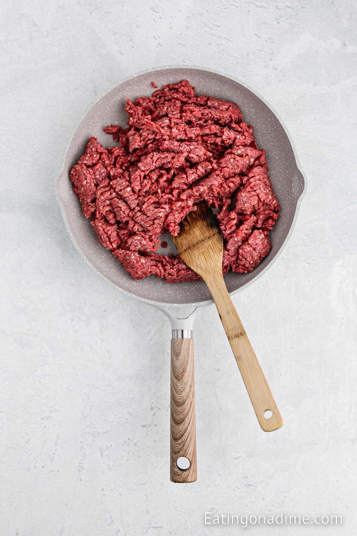 Cooking the ground beef in the skillet with a wooden spoon