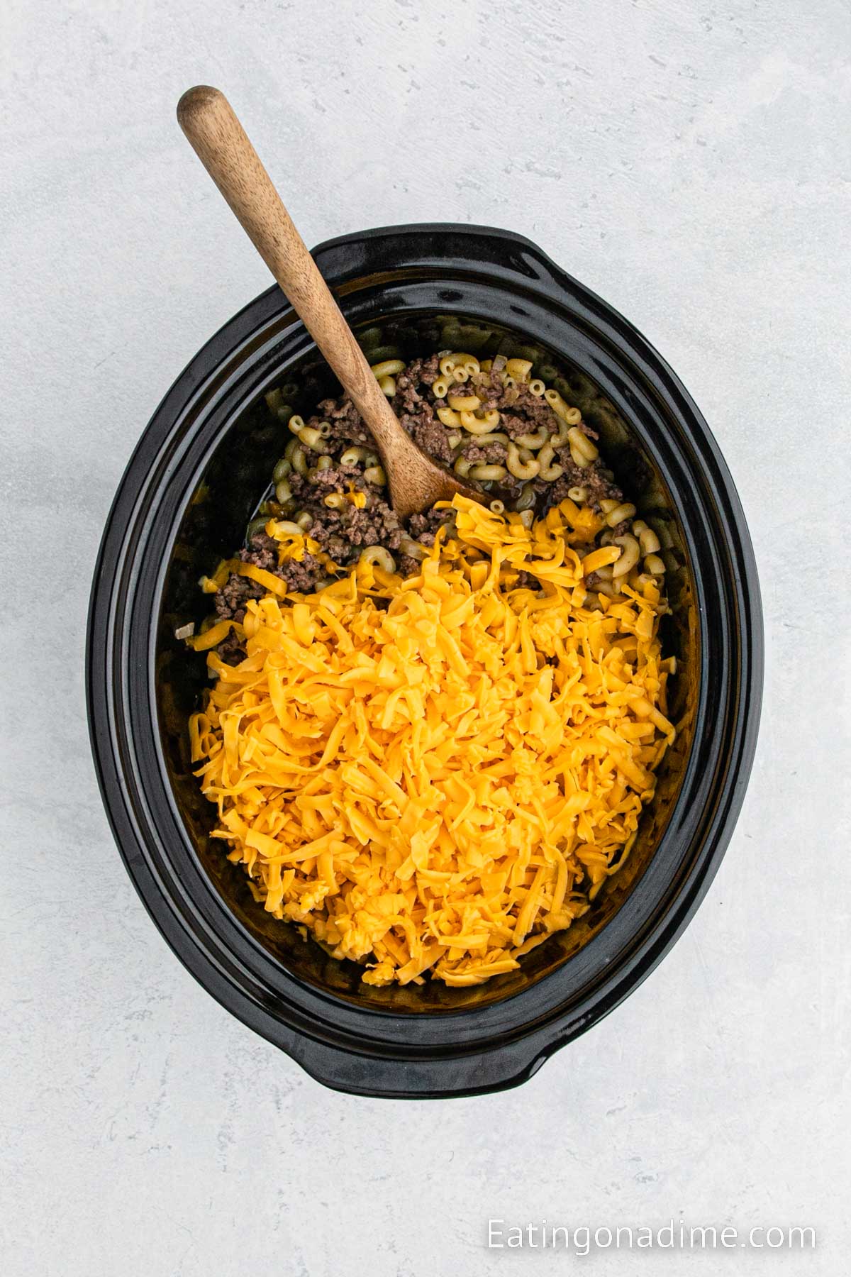 Topping the shredded cheese in the cheeeseburger mixture in the slow cooker with a wooden spoon