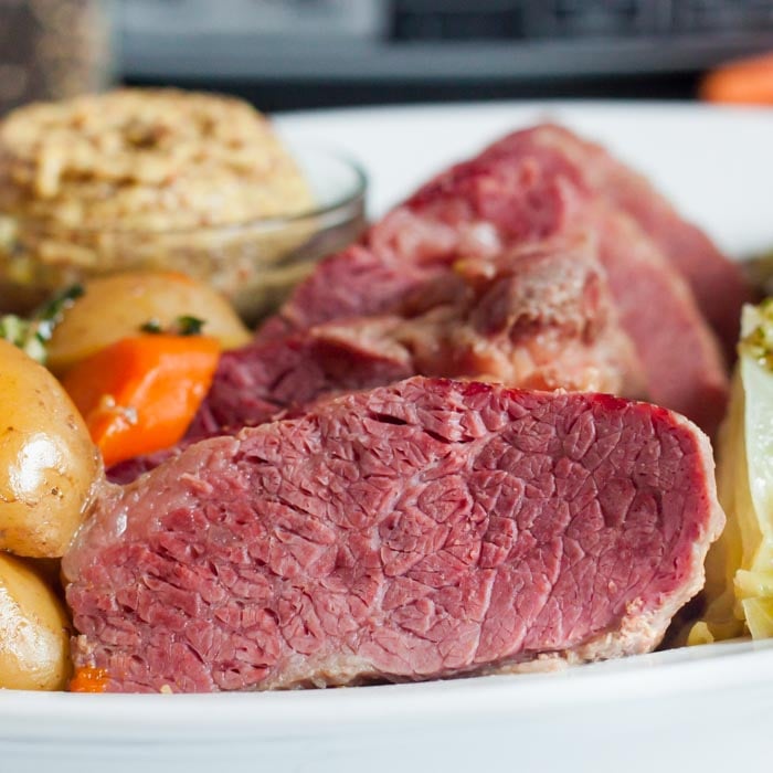 Close up of the sliced corned beef on a white plate next to cabbage, carrots and potatoes with a small bowl of spicy mustard on the plate.  