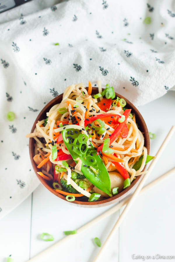 Close up image of chicken chow mein in a brown bowl with chopsticks on a table. 