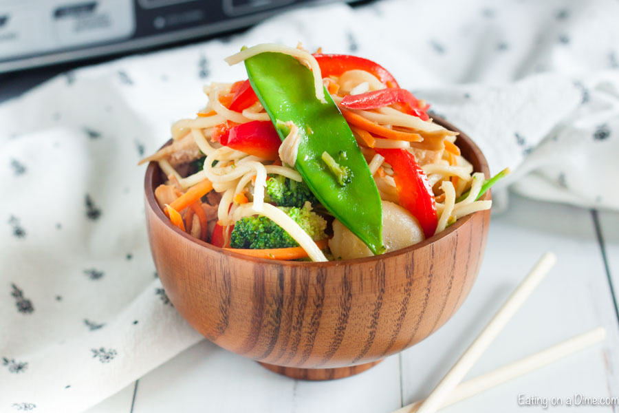 Close up image of chicken chow mein in a brown bowl on a table. 