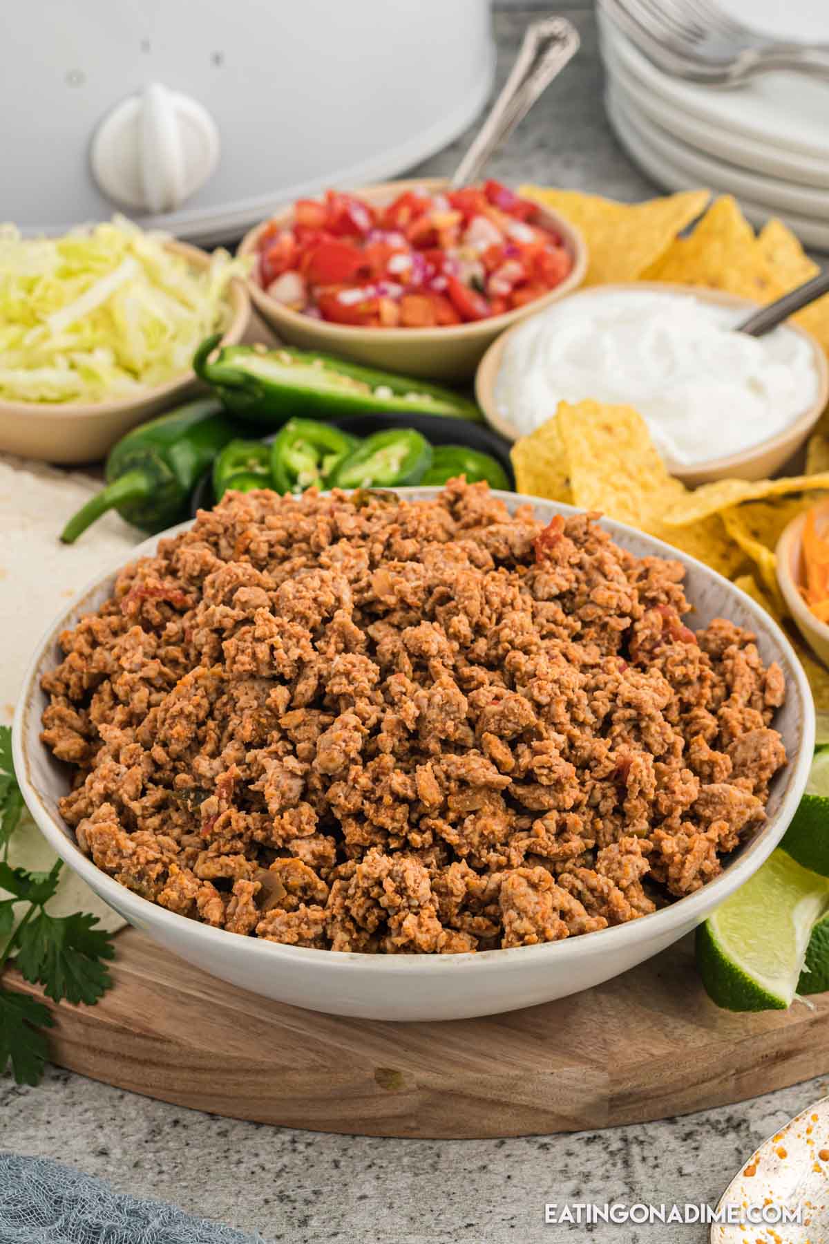 A bowl of ground chicken taco meat with a side bowl of lettuce, tomatoes and sour cream with chips and jalapenos