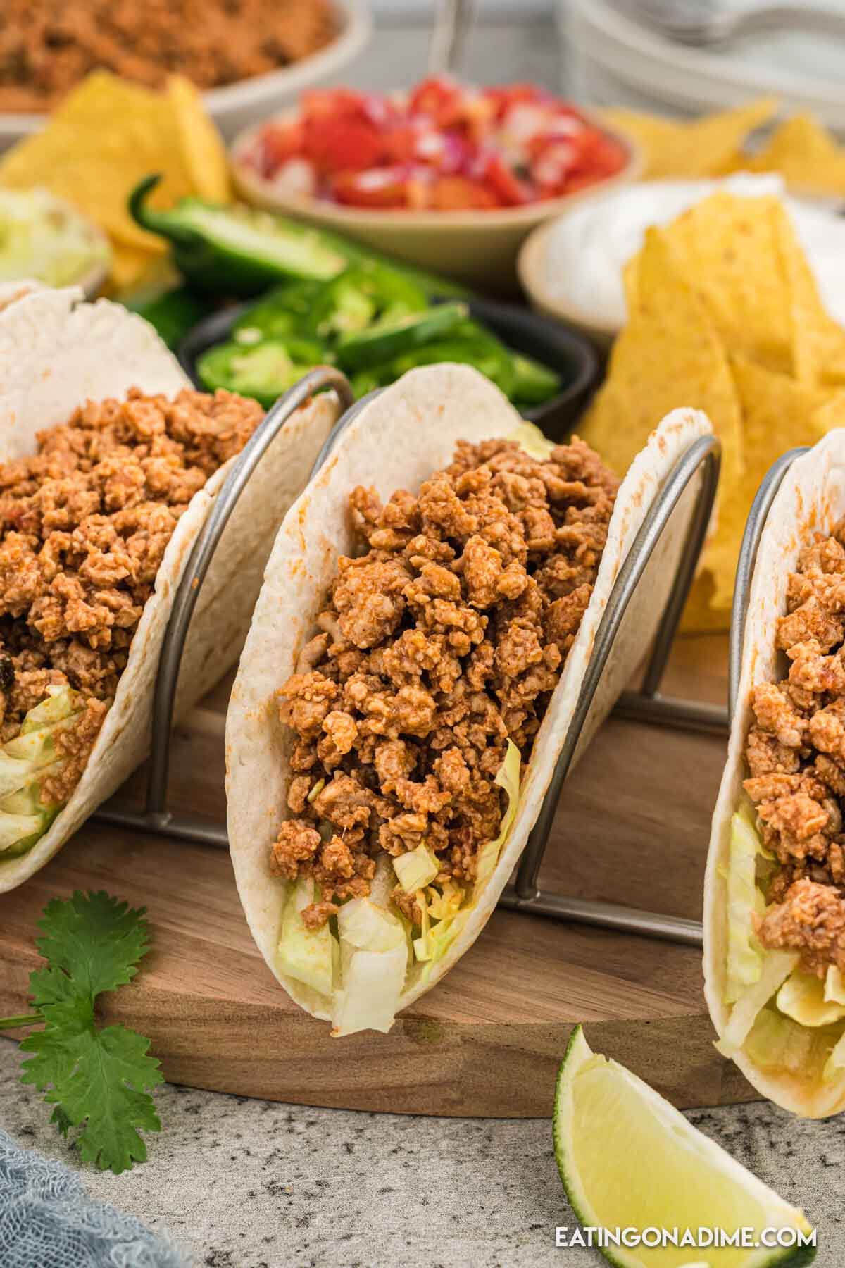 Ground Chicken Tacos in a taco stand with bowls of tomatoes jalapenos and chips on the side