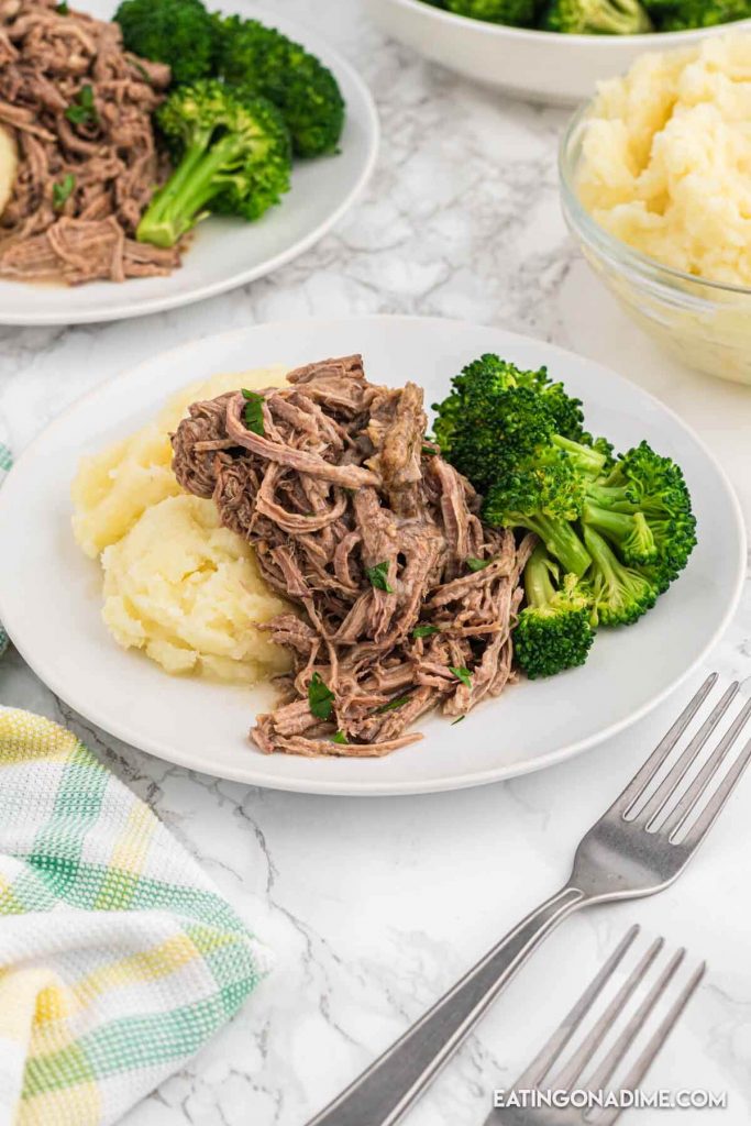Close up image of shredded beef on a plate with mashed potatoes and broccoli
