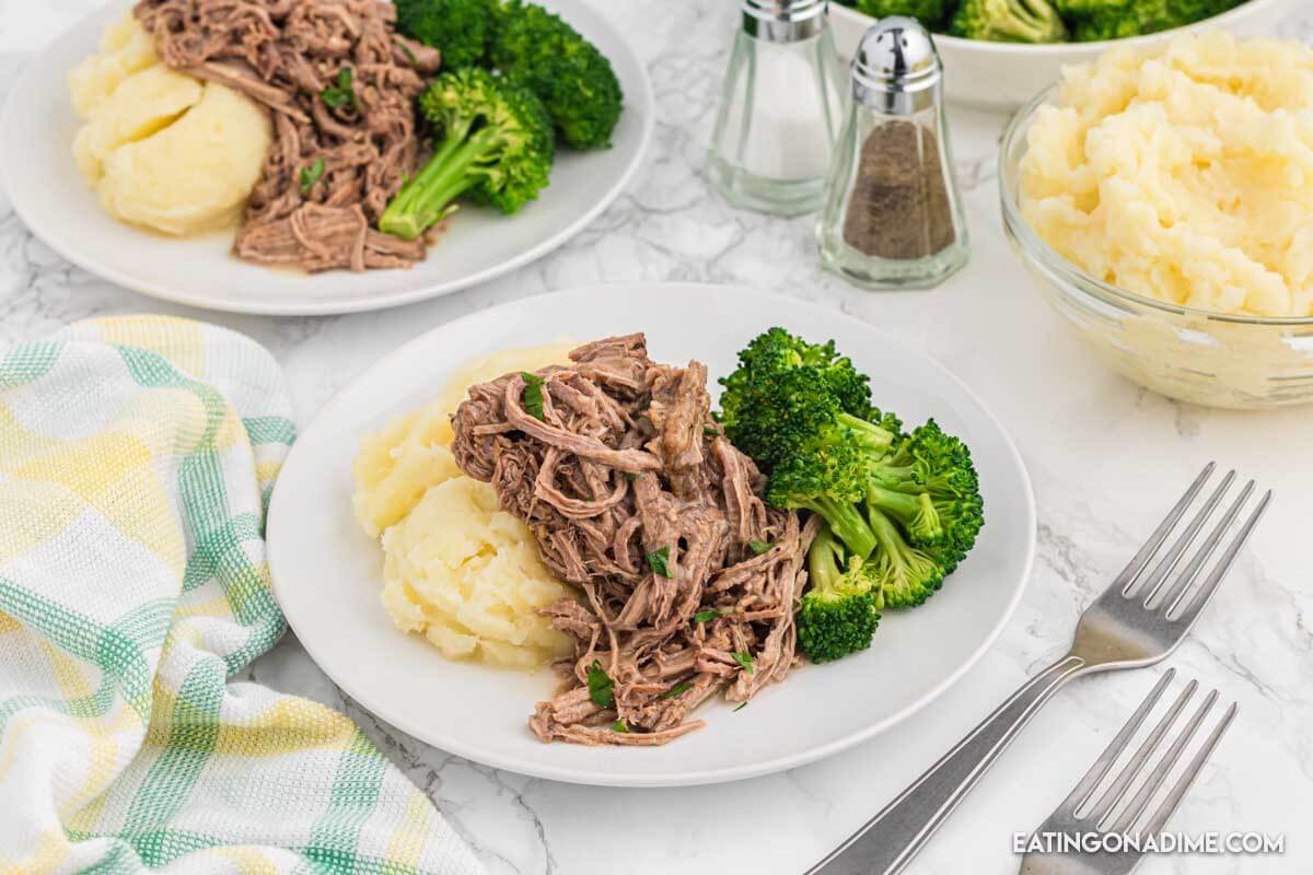 Close up image of shredded beef on a plate with mashed potatoes and broccoli