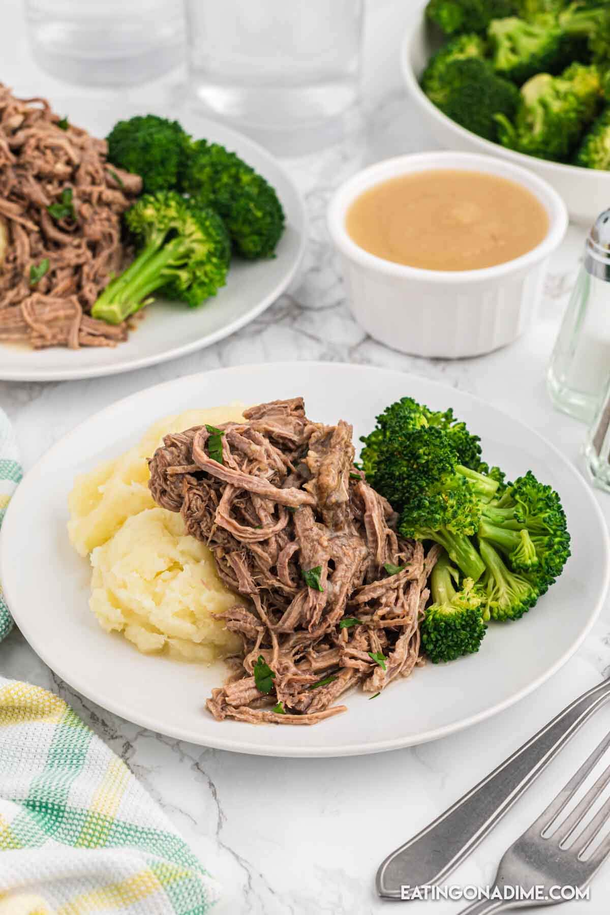 Close up image of shredded beef on a plate with mashed potatoes and broccoli