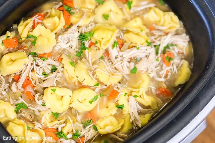 close up of a crock pot full of Chicken Tortellini soup topped with fresh parsley. 