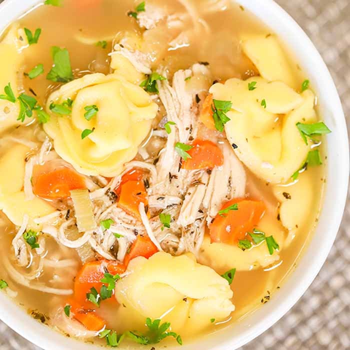 Close up of a bowl of Chicken Tortellini soup topped with fresh parsley. 