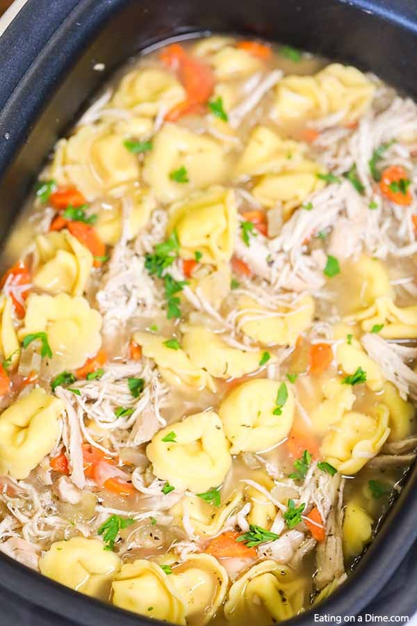 A crock pot full of Chicken Tortellini soup topped with fresh parsley. 