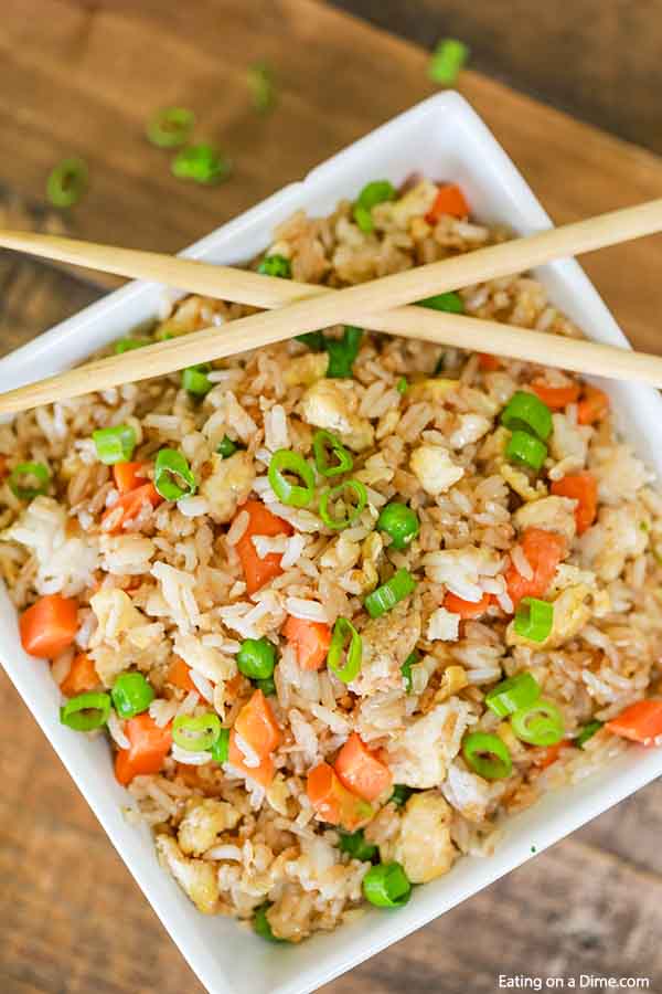 Close up of a large bowl of fried rice topped with green onions with chop sticks on top.  