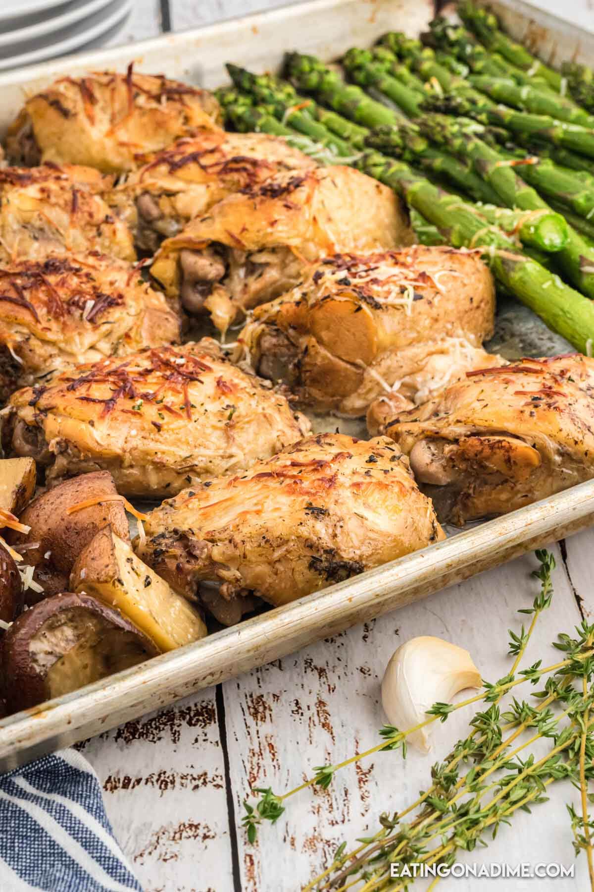 Chicken thighs, asparagus, potatoes on a baking sheet.