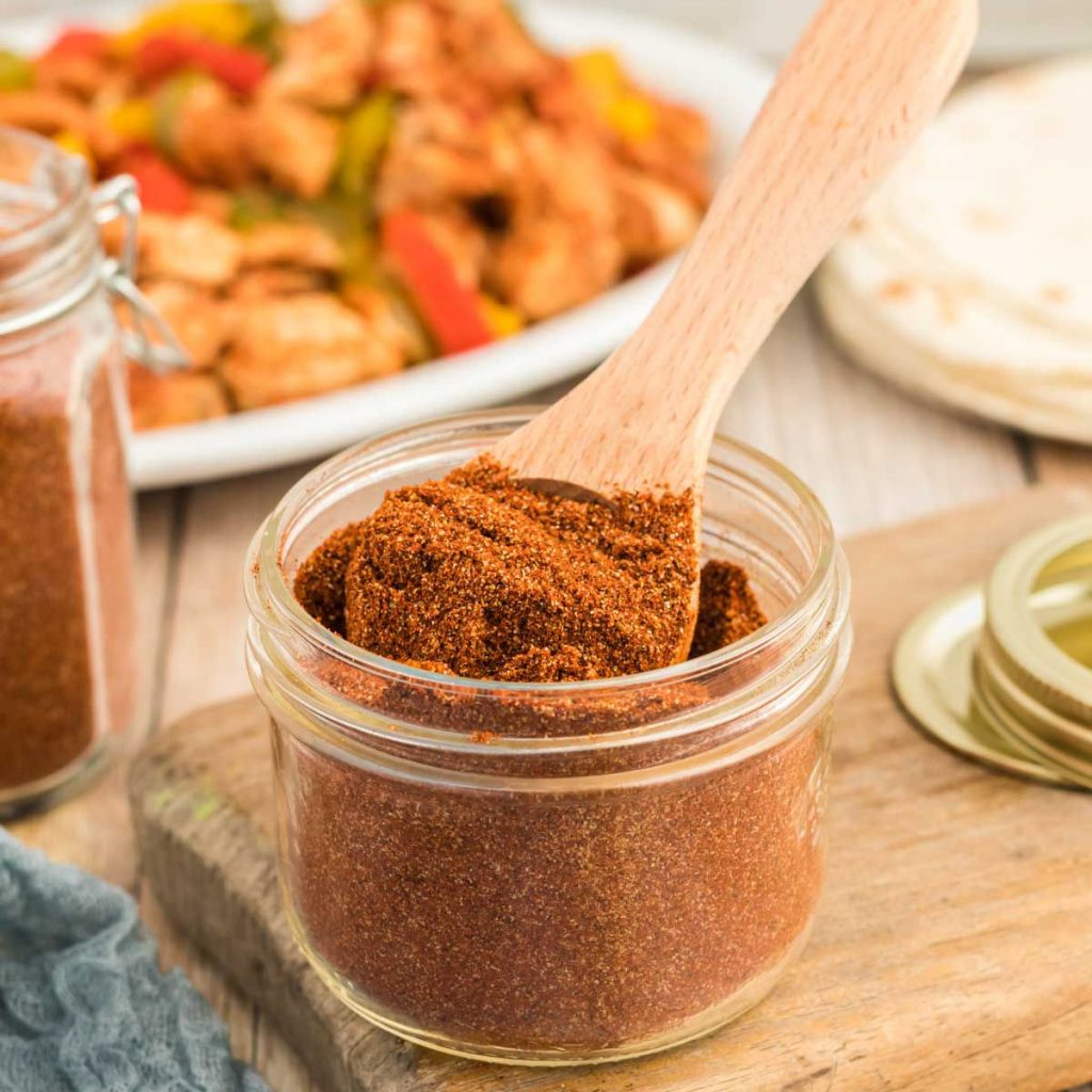Close up image of fajita seasoning in a jar with a teaspoon