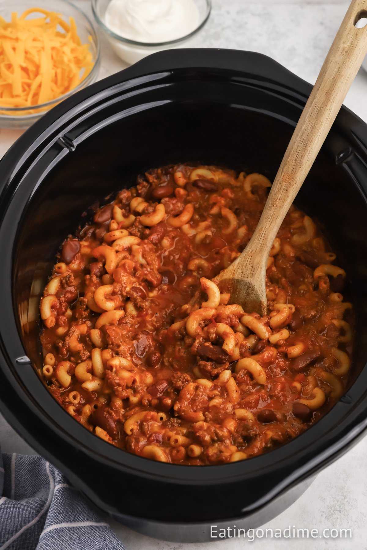 Chili Mac and Cheese in a slow cooker with a wooden spoon