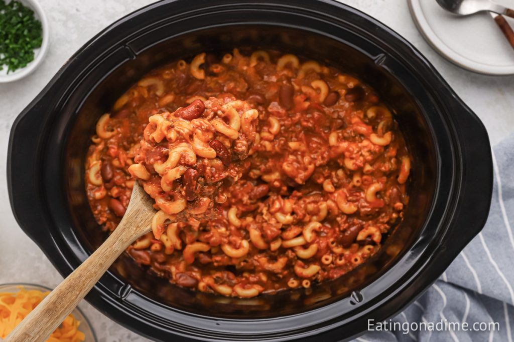 Chili Mac and Cheese in the slow cooker with a wooden spoon