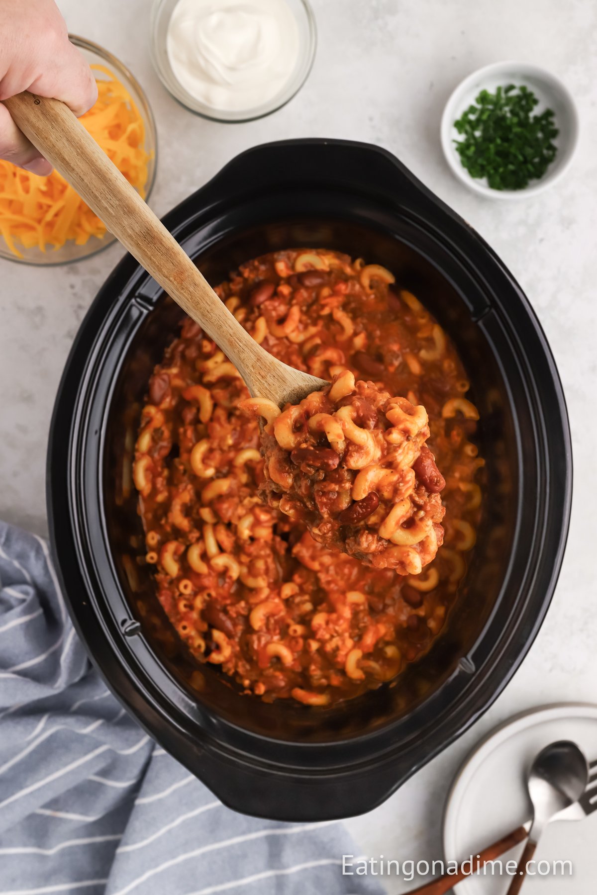 Chili Mac and Cheese in the slow cooker with a wooden spoon