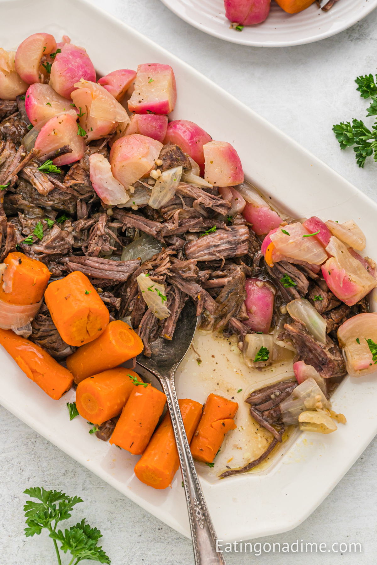 A platter of pot roast with carrots and onions and radishes with a serving spoon