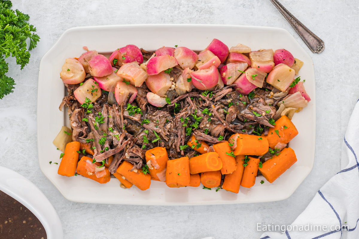 A platter with shredded pot roast, radishes, onions, and carrots