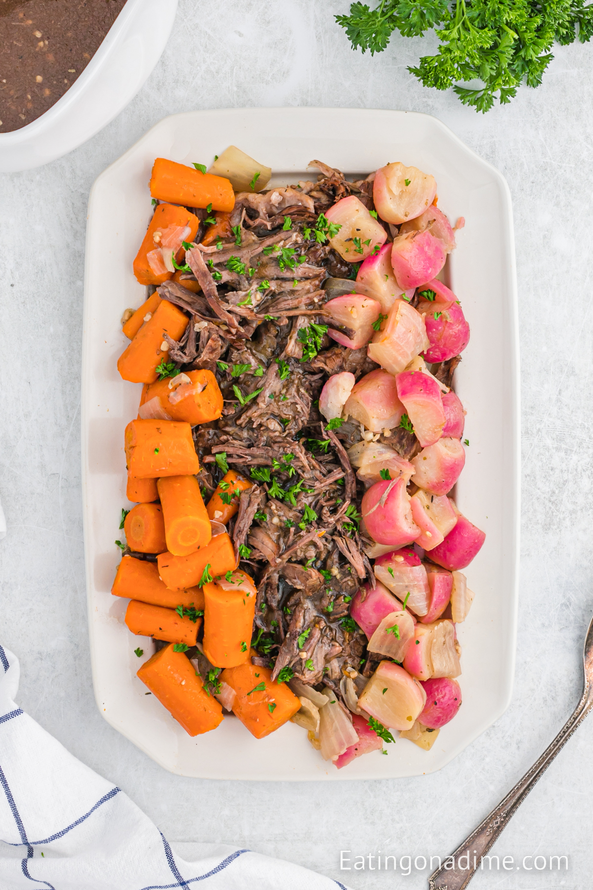 A platter with pot roast, carrots and radishes and onions