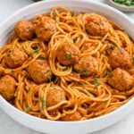 A white bowl filled with instant pot spaghetti and meatballs in tomato sauce, garnished with chopped parsley.