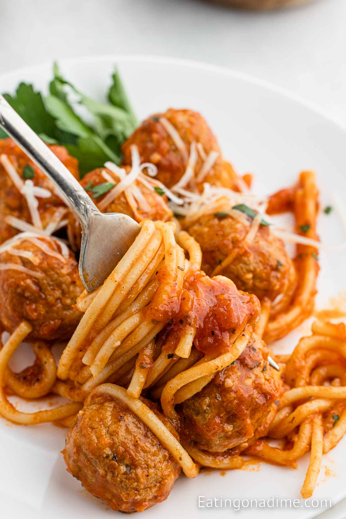 A serving of spaghetti and meatballs on a plate with a side of salad