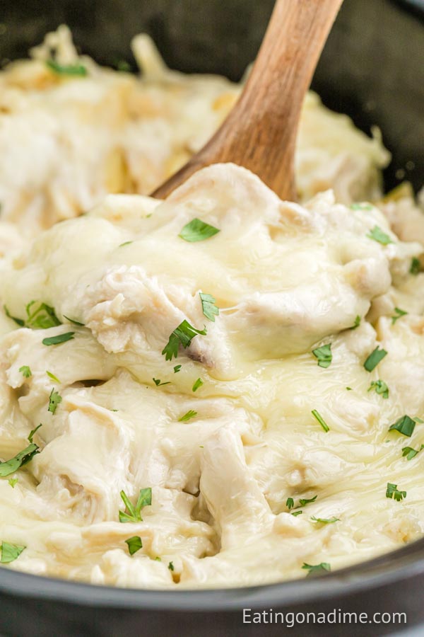 Close up image of Chicken Alfredo Casserole in the crock pot with a wooden spoon