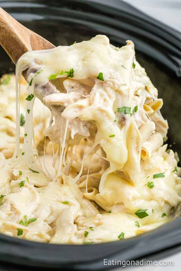 Close up image of Chicken Alfredo Casserole in the crock pot with a serving on a wooden spoon