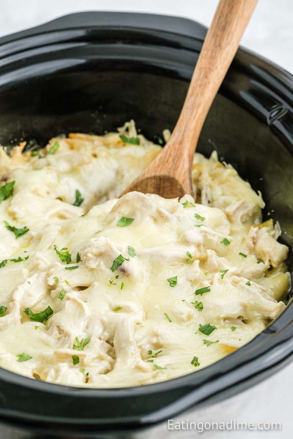 Close up image of Chicken Alfredo Casserole in the crock pot with a wooden spoon