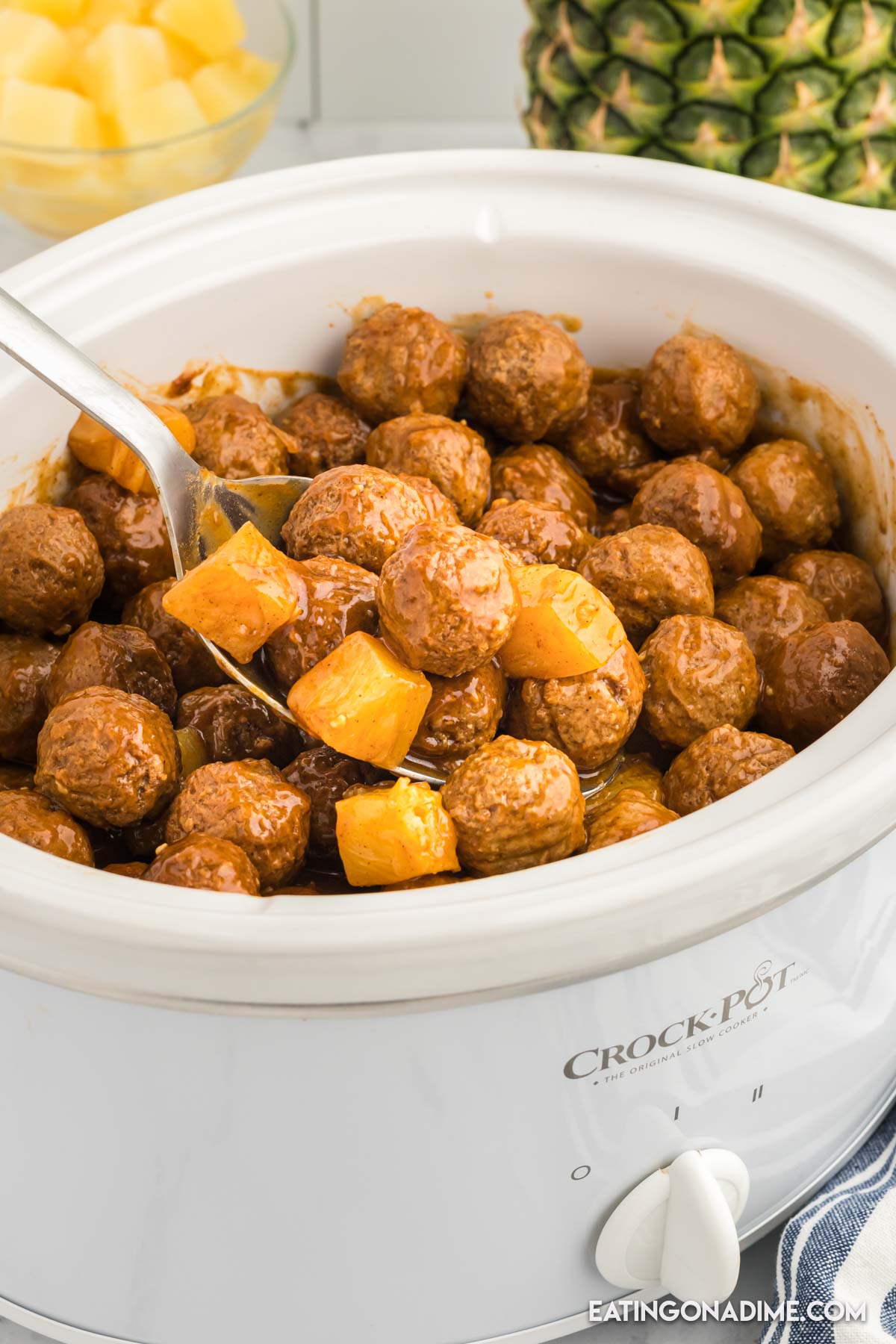 Slow cooker of Hawaiian BBQ Meatballs with a serving on a spoon