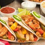 Three chicken fajita tacos made with our Instant Pot Chicken Fajitas Recipe, featuring grilled chicken, red and yellow bell peppers, and jalapeño slices in flour tortillas. Served with lime wedges, salsa, and sour cream in the background.