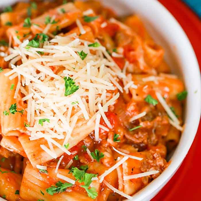 Close up image of Italian Sausage Rigatoni in a white bowl on a red plate. 