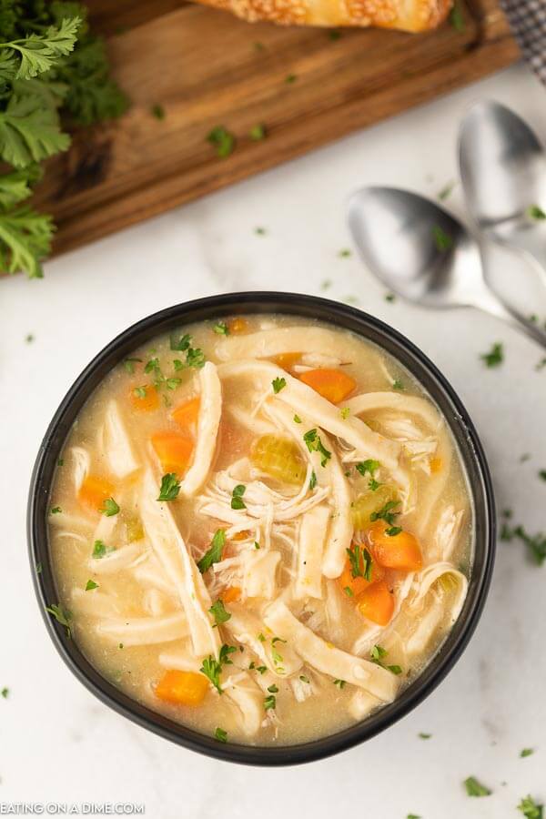 Close up image of chicken noodle soup in a black bowl with two spoons. 