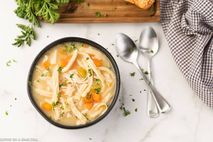 Image of a chicken noodle soup in a black bowl with two spoons on a table. 